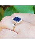 Women's 14k yellow gold ring with emerald-cut blue sapphire and diamond halo.