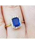A 14k yellow gold ring featuring a natural blue sapphire, beautifully encircled by a halo of natural diamonds, resting gracefully on a finger.