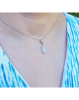 Necklace with a teardrop-shaped opal pendant worn by a person in a blue and white patterned top.