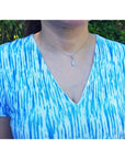 Person wearing an opal pendant in a blue and white tie-dye shirt with a blurred green background.