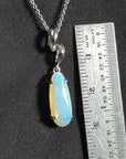 Opal pendant on a chain with a ruler for scale against a black background