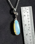 1.56 ct bluish-green opal pendant in 14K white gold, elongated pear shape, next to a ruler.