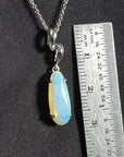 1.56 ct bluish-green opal pendant in 14K white gold, elongated pear shape, next to a ruler.