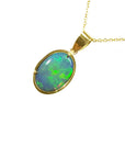 A bluish green opal pendant on a gold chain against a white background