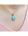 Oval bluish-green Australian opal pendant in 14K yellow gold, worn on a delicate chain.
