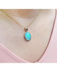Oval bluish-green Australian opal pendant in 14K yellow gold, worn on a delicate chain.