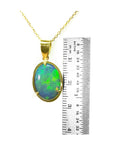 Opal pendant on a gold chain with a ruler for scale on a white background