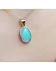 Oval bluish-green Australian opal pendant in 14K yellow gold, worn on a delicate chain.