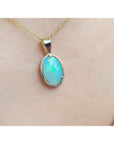 Oval bluish-green Australian opal pendant in 14K yellow gold, worn on a delicate chain.