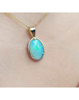 Oval bluish-green Australian opal pendant in 14K yellow gold, worn on a delicate chain.
