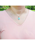Person wearing a pink top with a necklace featuring a natural opal pendant outdoors.