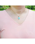 Natural Australian opal pendant with bluish green oval opal in 14K yellow gold, worn on a peach top.