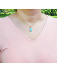 Natural Australian opal pendant with bluish green oval opal in 14K yellow gold, worn on a peach top.