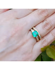 14K gold bridal emerald ring set with matching diamond wedding band on a hand.