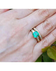 14K gold bridal emerald ring set with matching diamond wedding band on a hand.