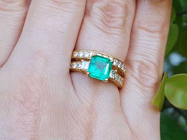 A close-up of emerald and diamond ring with match wedding band on a person's figer.
