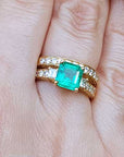 A close-up of emerald and diamond ring with match wedding band on a person's figer.