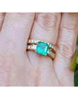 A close-up of emerald and diamond ring with match wedding band on a person's figer.