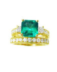A top view of an emerald ring with accent diamonds and matching band in yellow gold, sideways profile.