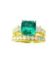 A top view of an emerald ring with accent diamonds and matching band in yellow gold, sideways profile.