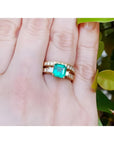 14K gold bridal emerald ring with matching diamond wedding band on a finger.