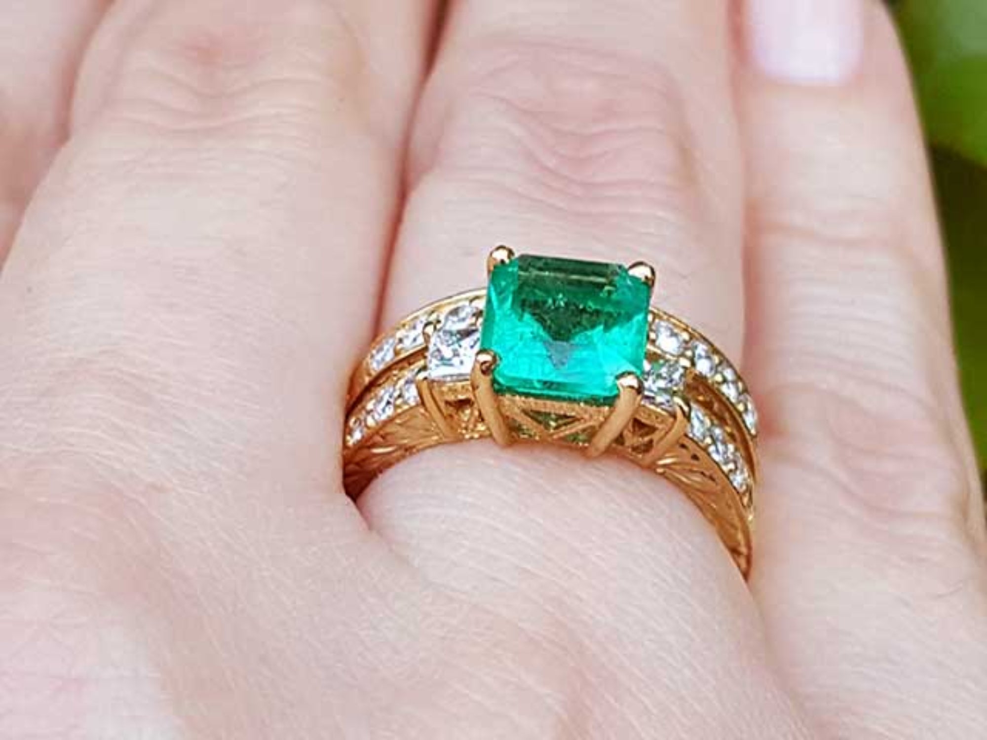 Gold ring with a square emerald on a finger.