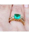 Gold ring with a square emerald on a finger.