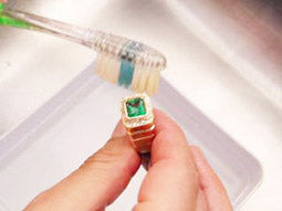 Brushing emerald ring on top side main gemstone and accent diamonds removing dirt