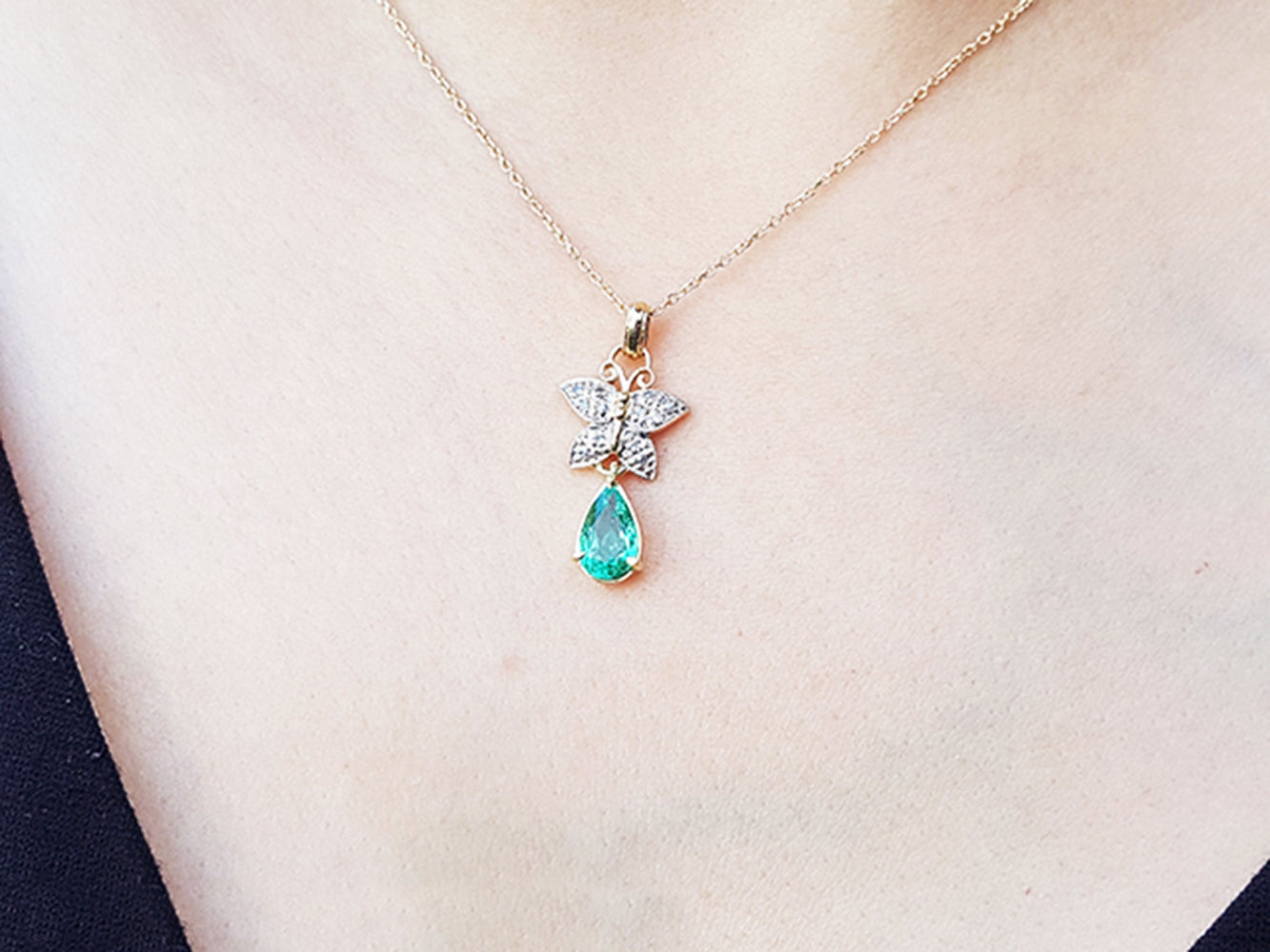 Necklace with a natural emerald teardrop pendant and butterfly design on a plain skin background.