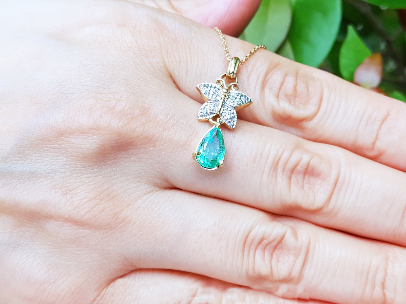 Gold necklace with a green teardrop pendant held in a hand against a blurred green background