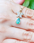 Gold necklace with a green teardrop pendant held in a hand against a blurred green background