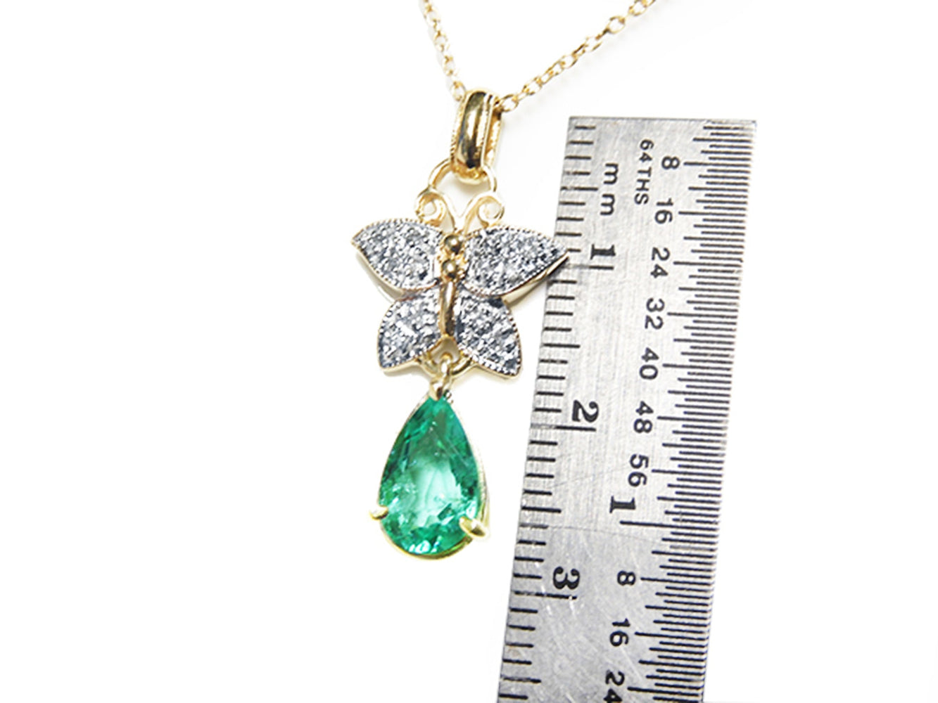 Gold pendant with emerald teardrop gemstone and butterfly design, next to a ruler for scale.