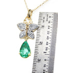 Gold pendant with emerald teardrop gemstone and butterfly design, next to a ruler for scale.