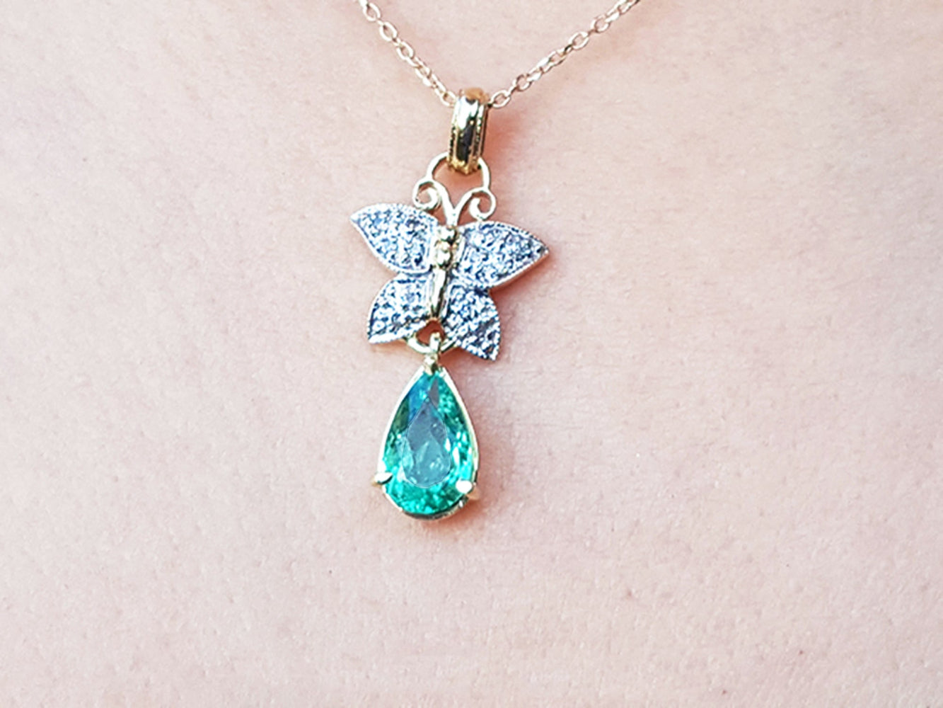 Necklace with a butterfly and teardrop-shaped gemstone pendant on a light pink background