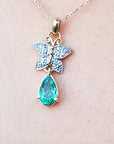 Necklace with a butterfly and teardrop-shaped gemstone pendant on a light pink background