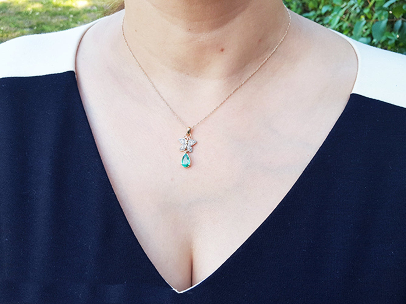 Necklace with a butterfly emerald pendant worn by a person against a blurred natural background.