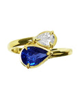 A 18k yellow gold bypass ring toi et moi design a pear-cut blue sapphire and a smaller pear-cut diamond.