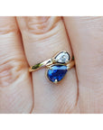 Two-stone "You and Me" blue natural sapphire bypass ring featuring a sparkling medium-deep blue teardrop diamond on the side, handcrafted in 18k yellow gold.