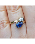 Two-stone "You and Me" blue natural sapphire bypass ring featuring a sparkling medium-deep blue teardrop diamond on the side, handcrafted in 18k yellow gold.