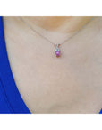 Necklace with a pink sapphire pendant on a person wearing a blue top.