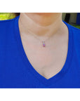 Person wearing a blue shirt with a necklace featuring a small pink sapphire pendant.