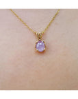 Gold necklace with a pink sapphire solitaire pendant on a skin background.