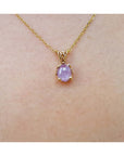 Gold necklace with a pink sapphire solitaire pendant on a skin background.