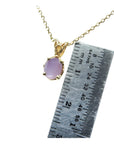Gold necklace with a pink sapphire solitaire pendant next to a ruler for scale.