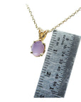 Gold necklace with a pink sapphire solitaire pendant next to a ruler for scale.