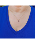 Person wearing a blue shirt with a gold necklace featuring a purple sapphire solitaire pendant.