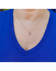 Person wearing a blue shirt with a gold necklace featuring a purple sapphire solitaire pendant.