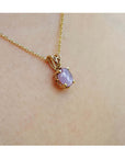 Gold necklace with a pink sapphire pendant on a person's neck.