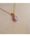 Gold necklace with a pink sapphire pendant on a person's neck.