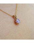 Gold necklace with a pink sapphire pendant on a person's neck.